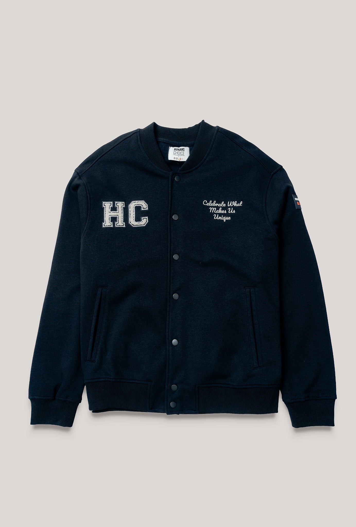 chamarra varsity azul marino de Humans Choice, de algodón de gramaje pesado, suave al tacto. Con parche bordado de lado derecho con las letras HC y bordado altura pecho del lado izquierdo con frase "Celebrate what makes us unique". Fit oversized con un look de streetwear